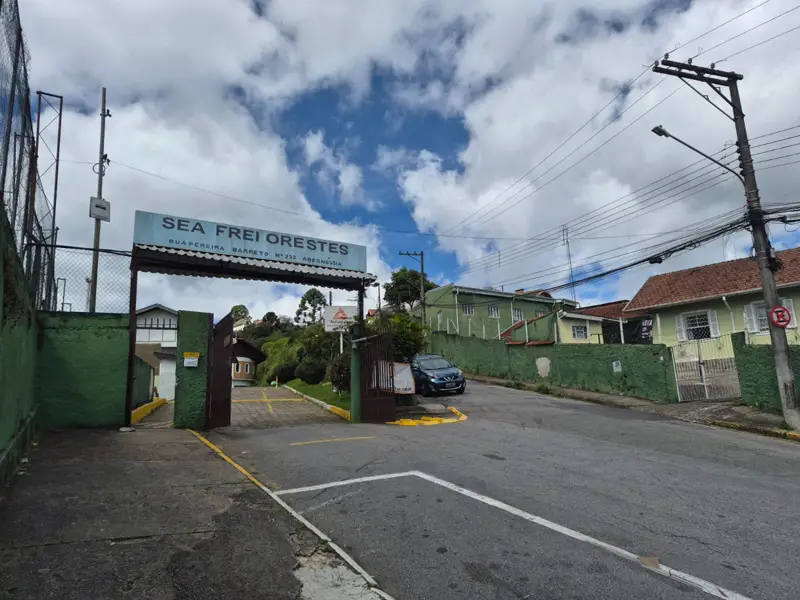 Portal de entrada da SEA Frei Orestes em Campos do Jordão, com a placa da instituição, portão aberto e muros verdes.